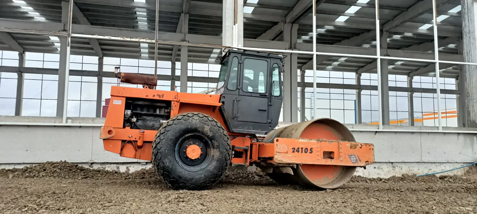 Kiralık Hamm 3410 toprak silindiri, kapalı fabrika yapısının içinde zemin dolgusunu sıkıştırırken; 12 ton sınıfı, 2,10 m düz tambur.